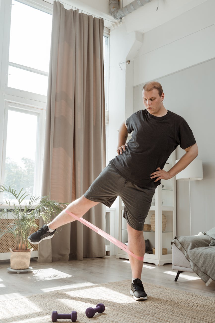 man in black t shirt and gray shorts doing leg exercises with rubber strength band